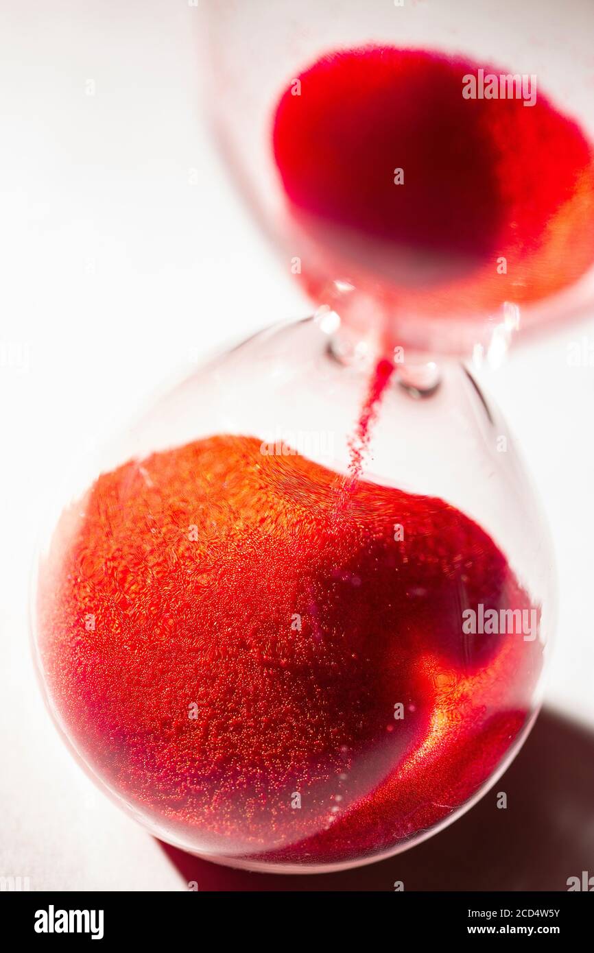 hourglass with red sand used to measure time flow, macro photography