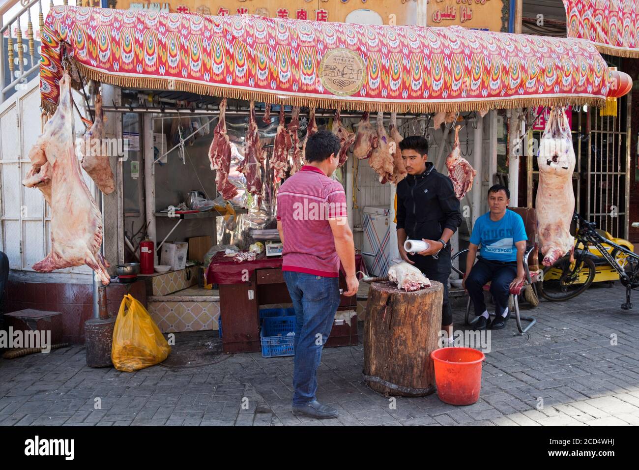 Uyghur street butcher selling pork's meat at butcher's shop / butchery in the city Kashgar / Kashi / Kasjgar, Xinjiang, China Stock Photo