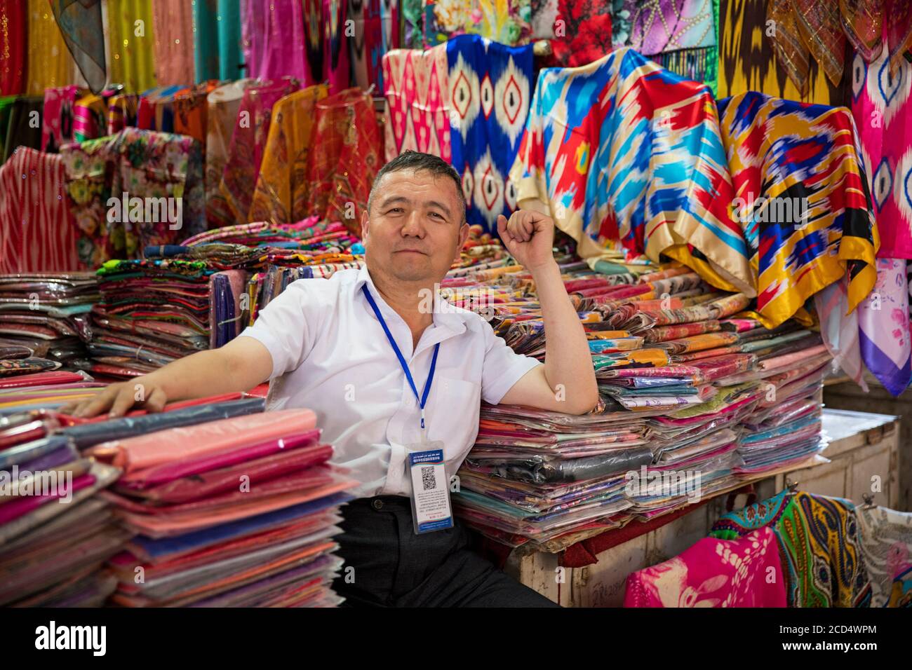 Uyghur vendor selling colourful cloth in fabric store / draper's shop in the city Kashgar / Kashi / Kasjgar, Xinjiang, China Stock Photo