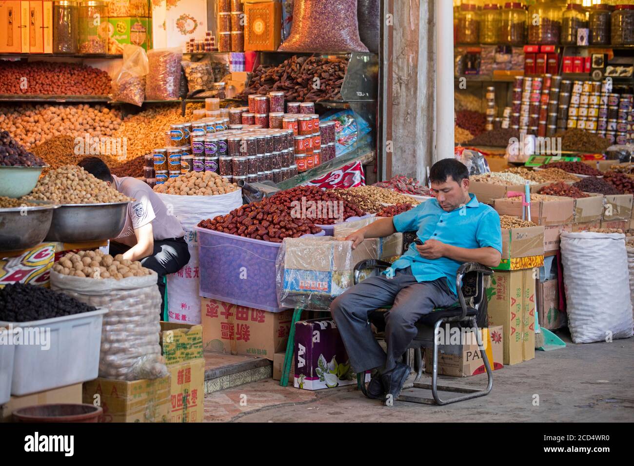 Uyghur vendor selling nuts and dried fruit in food shop in the city Kashgar / Kashi / Kasjgar, Xinjiang, China Stock Photo