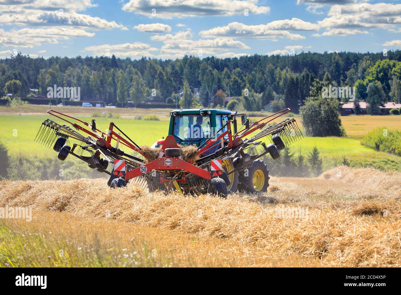 Farmer working on field with John Deere 6420S tractor and Fella rotary rake, raking dry straw on day of late summer. Salo, Finland. August 16, 2020. Stock Photo