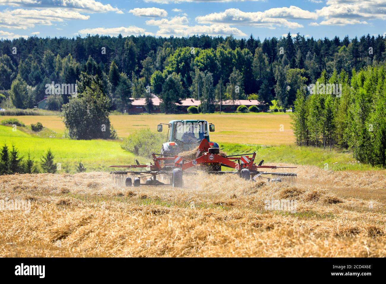 Farmer working in field with John Deere 6420S tractor and Fella rotary rake, raking dry straw on day of late summer. Salo, Finland. August 16, 2020. Stock Photo