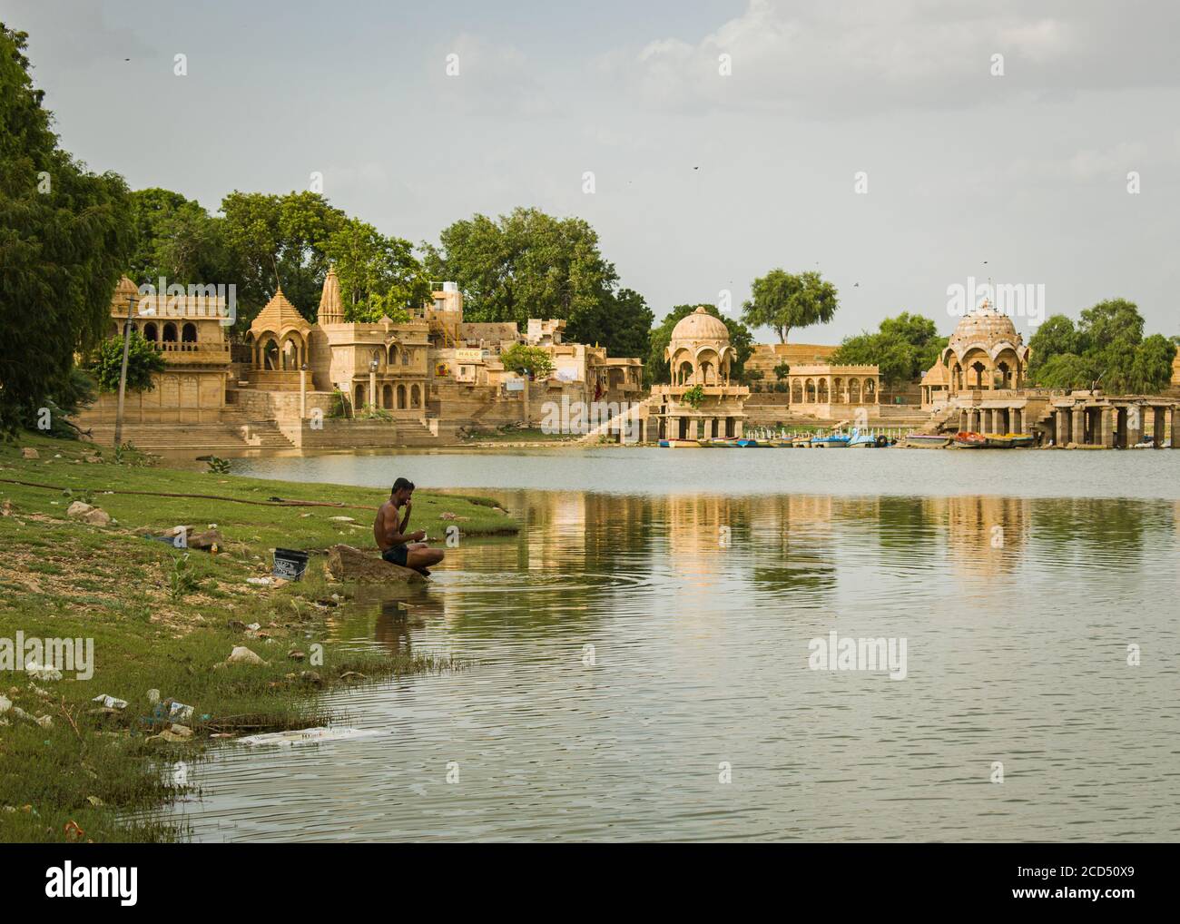 local middle aged man bathing and washing clothes at the shore of a dirty lake Stock Photo