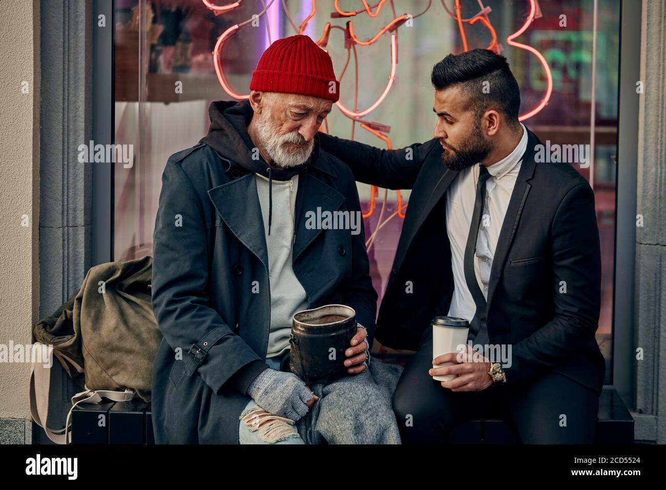 Rich man in tuxedo and homeless person in dirty clothes sitting and talking in the street. Poverty, help Stock Photo