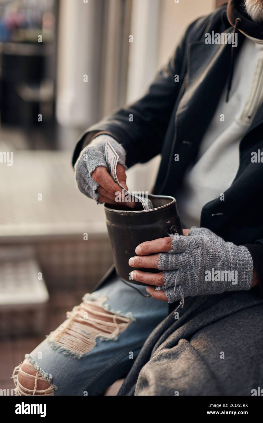 Pity hands of vagrant in grey gloves holding can for collecting money Stock Photo