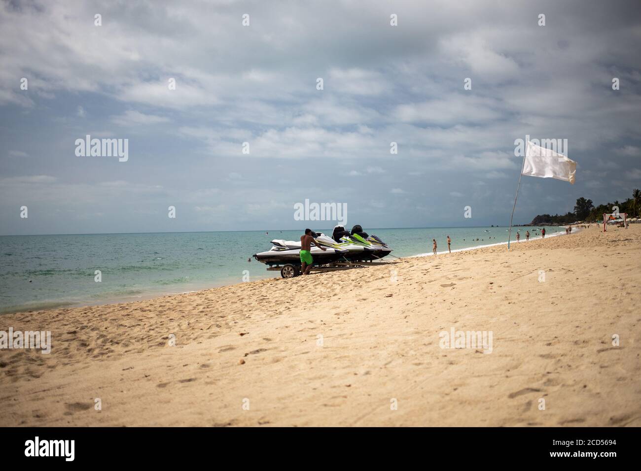 man loads on a trolley jet skis on a sandy beach on a background of the sea with waves. a white flag waving nearby with a place for a spear of space Stock Photo