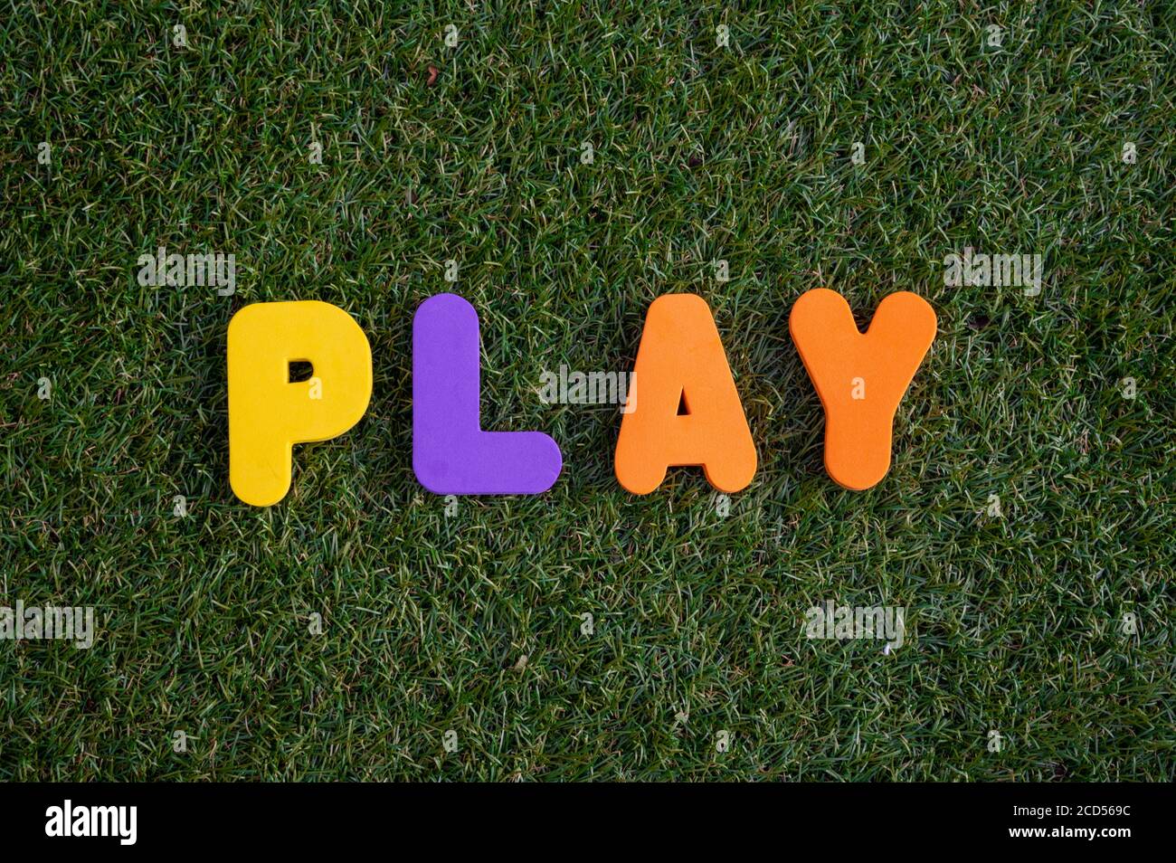 Capital letter 'Play' word from colorful of wood on grass background. Stock Photo
