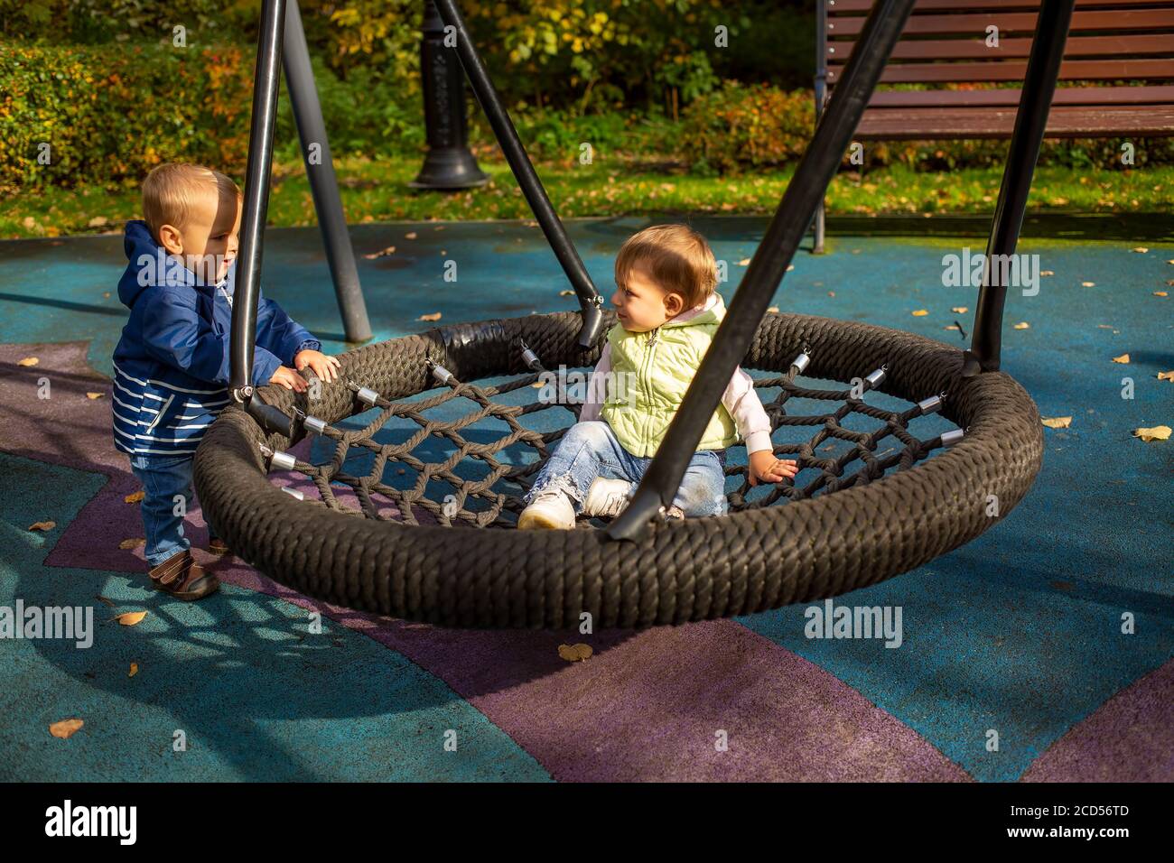 two toddlers a boy and a girl play cheerfully and swing on a swing hammock on a playground in the autumn park Stock Photo Alamy