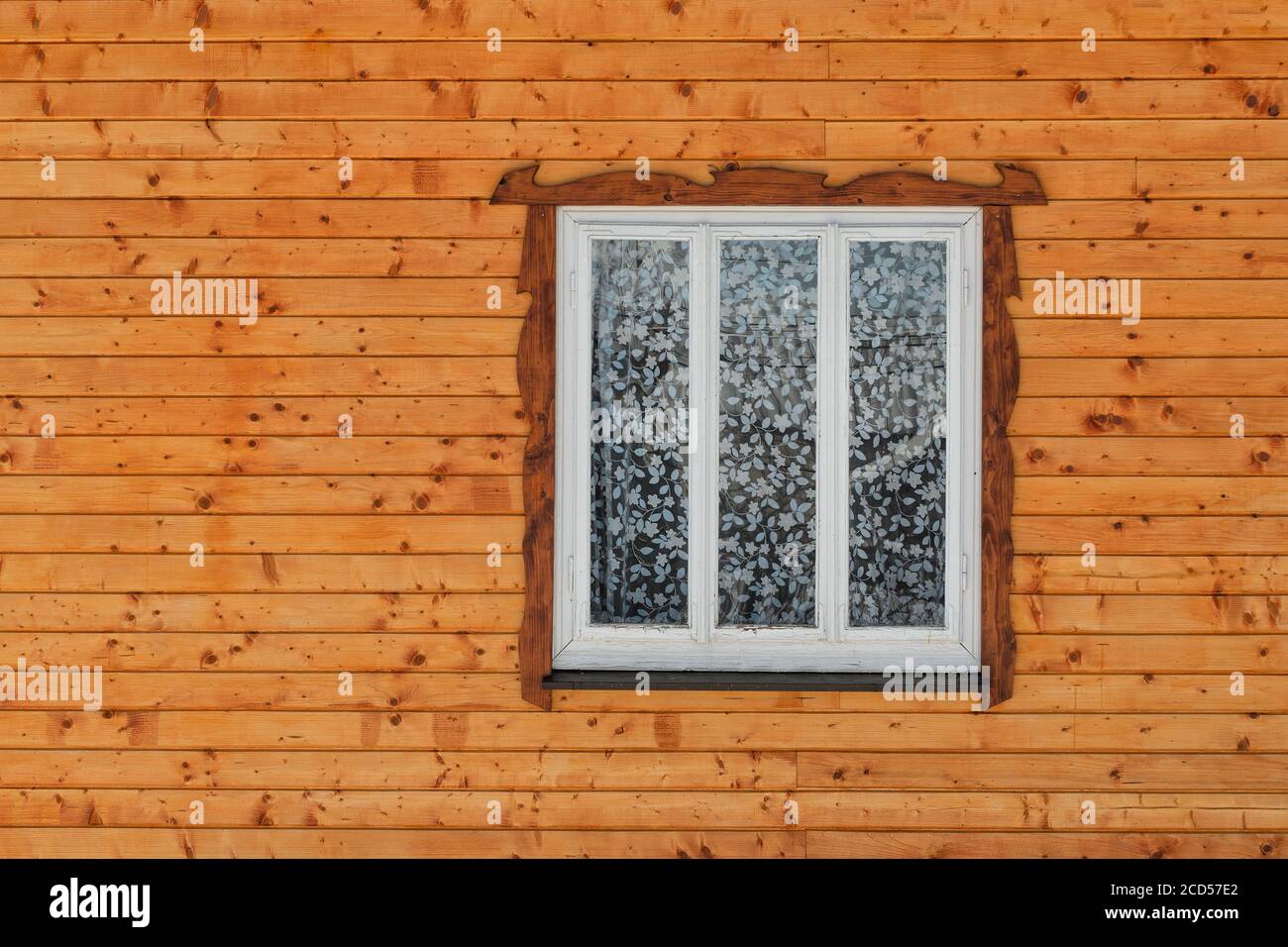 White wooden window in the wall of raw brown wooden planks with knots ...