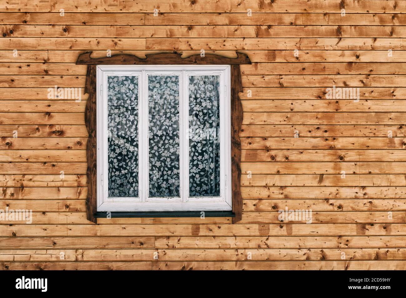 White wooden window in the wall of raw brown wooden planks with knots ...