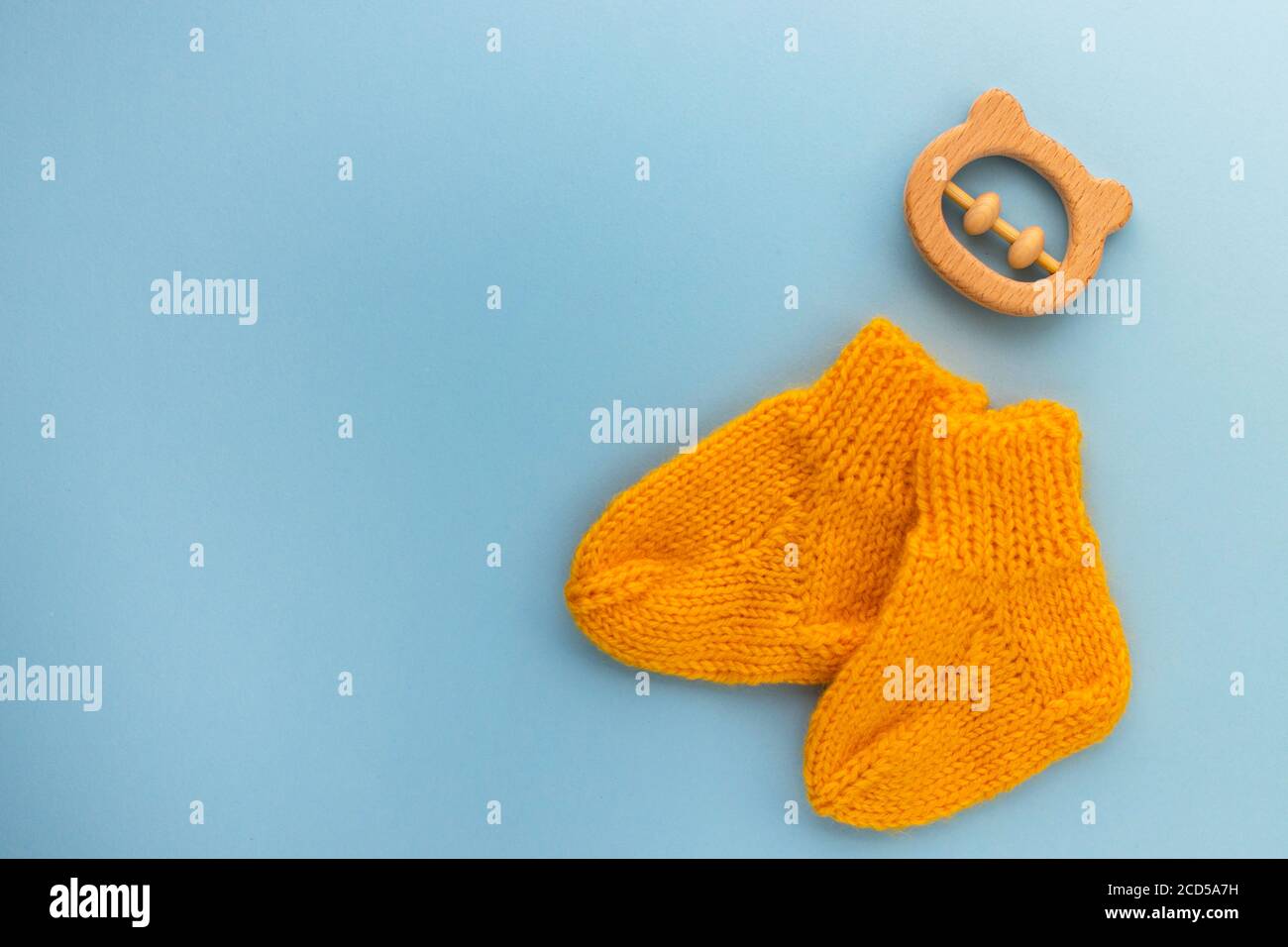 Pair of cute orange knitted baby socks and wooden teether bear on blue
