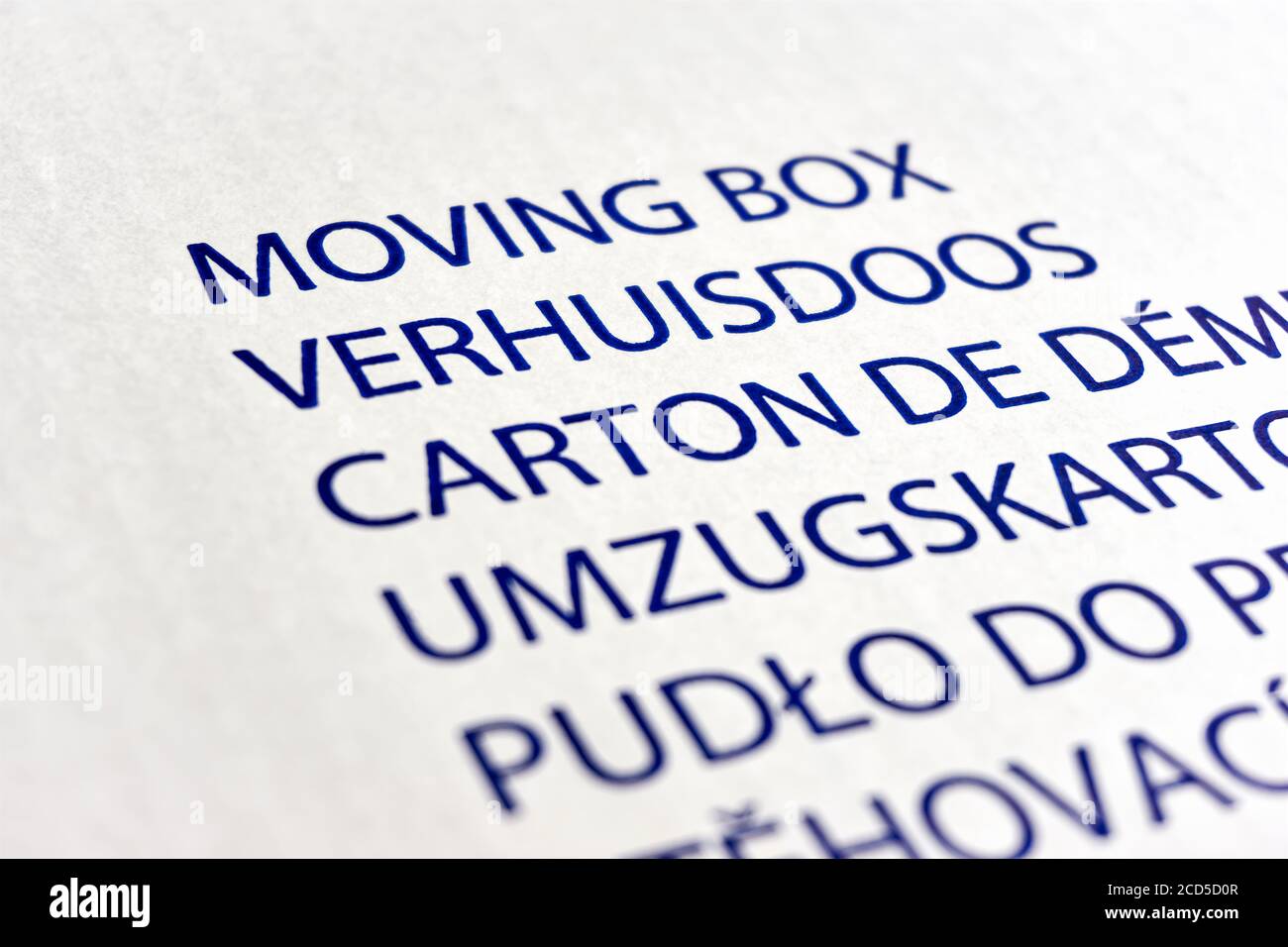 Closeup of white cardboard moving box with text in different languages. Moving, new house, new