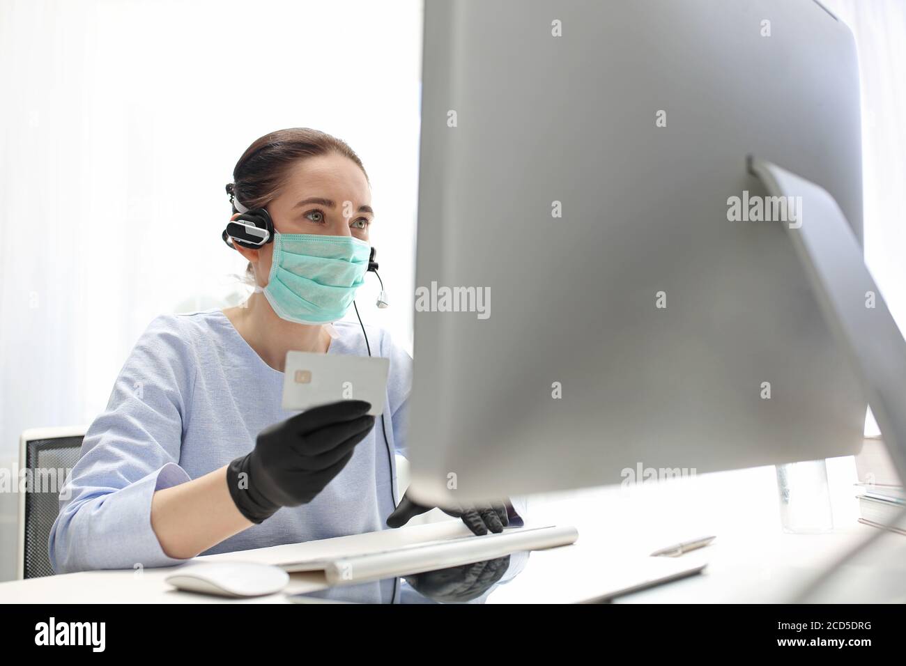 Remote work. A woman in a surgical mask works on the computer. Work during the plague Quarantine. Working at the computer in a mask. protection of emp Stock Photo