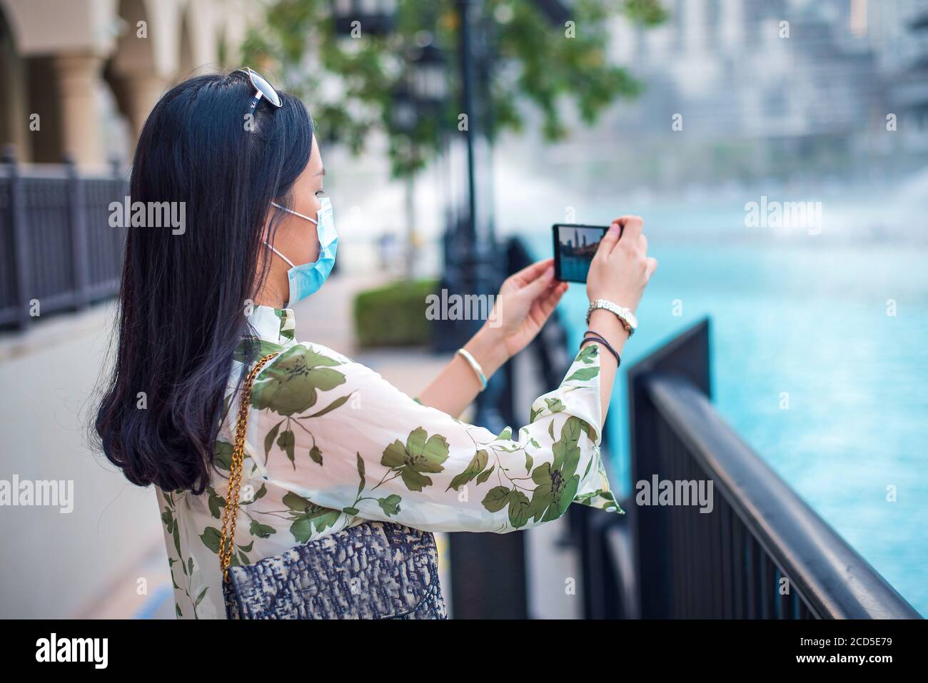 Happy female Asian tourist wearing face mask and taking photo at Dubai