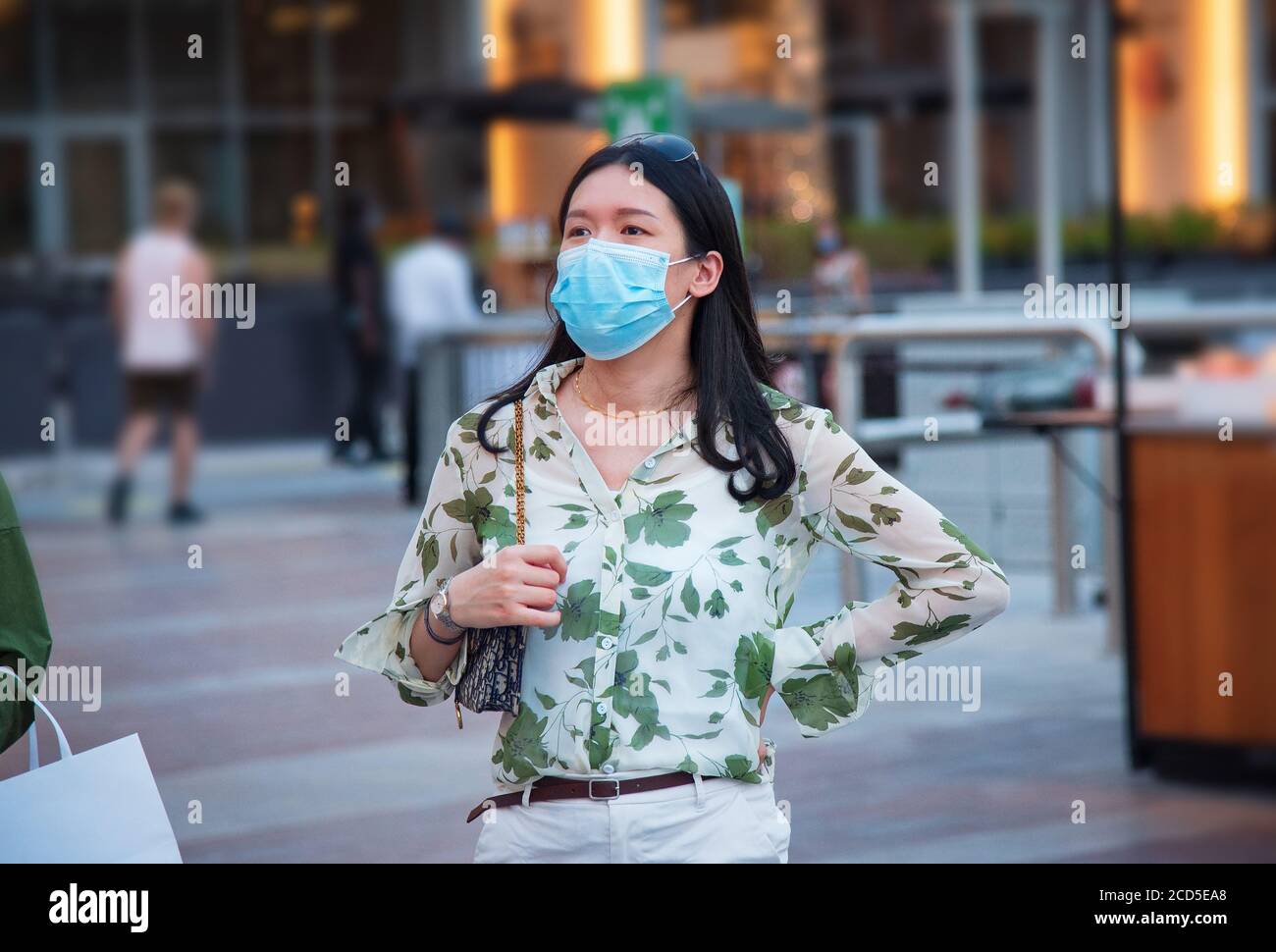 Asian woman wearing surgical face mask in outdoors area of a shopping mall in Dubai. Travel and leisure new normal after coronavirus Covid-19 pandemic Stock Photo