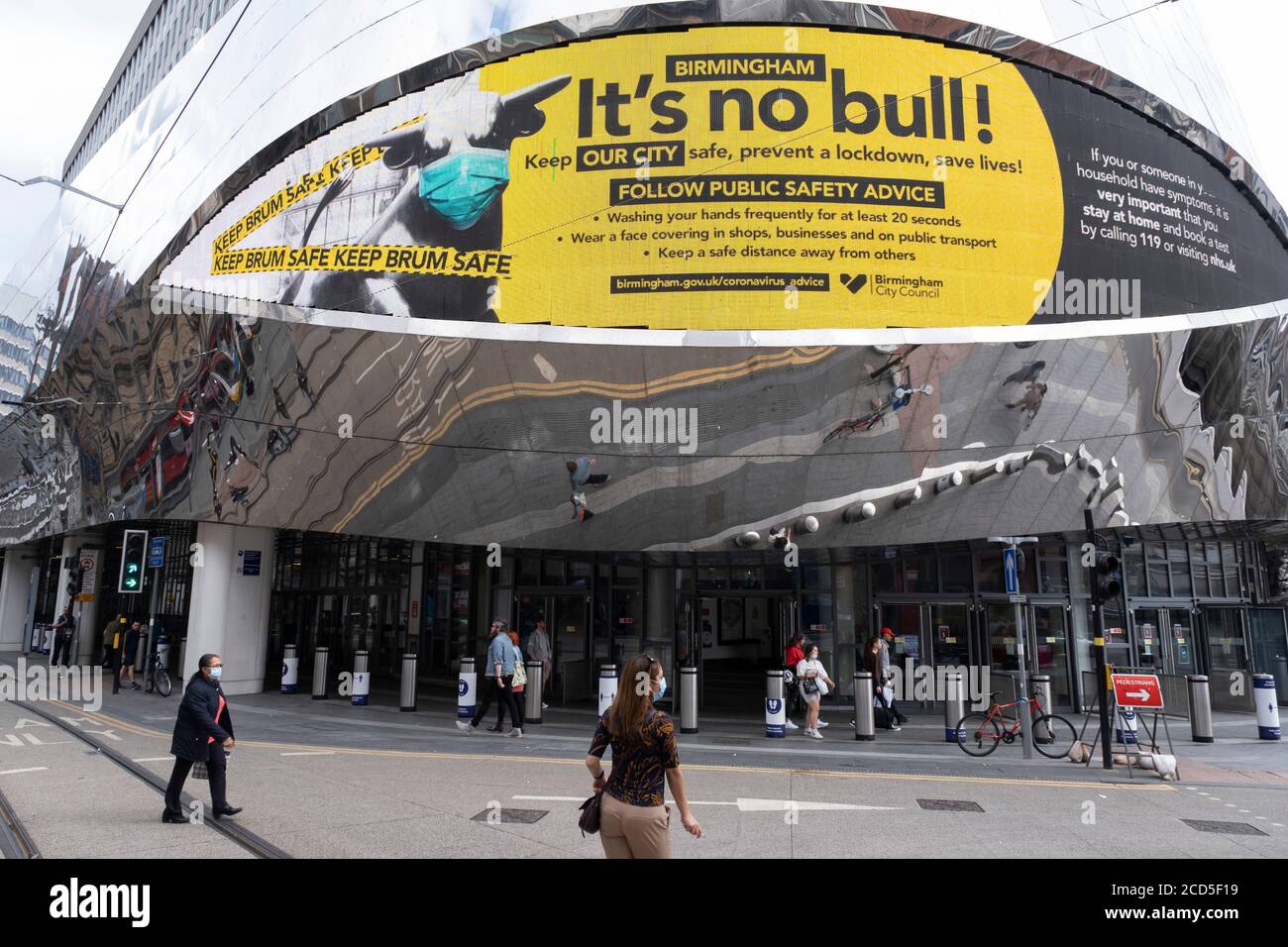 As numbers of Covid-19 cases in Birmingham have increased in recent weeks, and with the city added as an area of enhanced support on the UKs coronavirus watchlist of critical areas which are under threat of a local lockdown, people interact beneath a new public health advice advertising campaign featuring Bully the Bull Ring bull wearing a face mask with the slogan Its NO bull. Keep Brum safe outside Grand Central station in the city centre on 24th August 2020 in London, United Kingdom. With other areas in the Midlands under localised lockdown, people and businesses are being urged to follow t Stock Photo