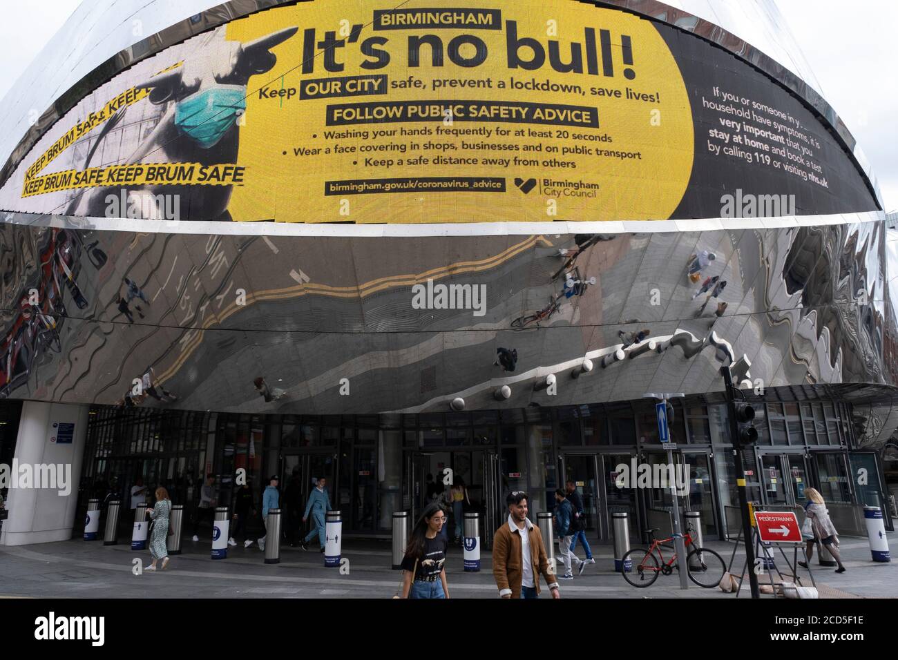 As numbers of Covid-19 cases in Birmingham have increased in recent weeks, and with the city added as an area of enhanced support on the UKs coronavirus watchlist of critical areas which are under threat of a local lockdown, people interact beneath a new public health advice advertising campaign featuring Bully the Bull Ring bull wearing a face mask with the slogan Its NO bull. Keep Brum safe outside Grand Central station in the city centre on 24th August 2020 in London, United Kingdom. With other areas in the Midlands under localised lockdown, people and businesses are being urged to follow t Stock Photo