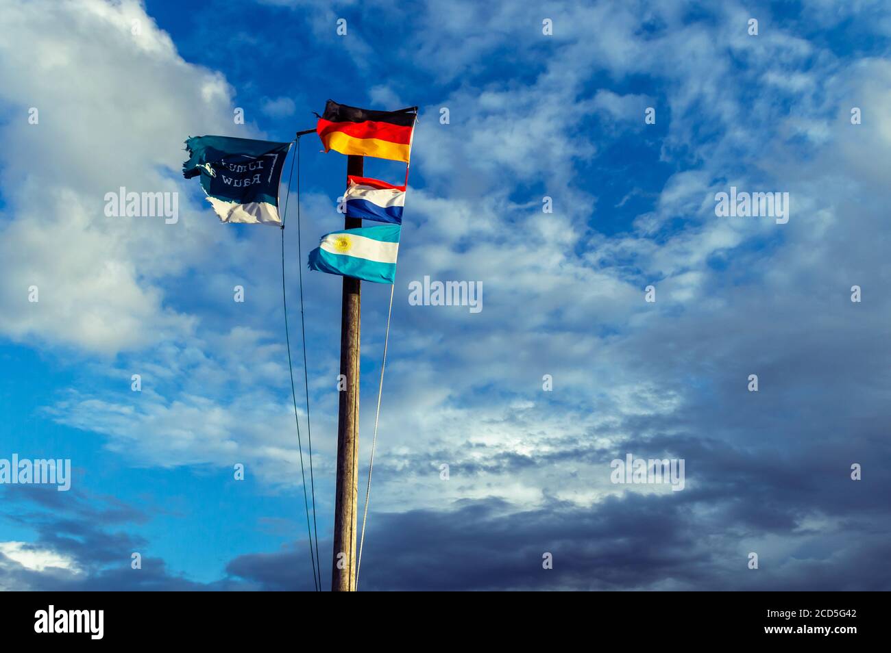 Wooden flagpole with the German, Dutch and the Argetina flag. And the welcome flag of the little Dutch town Ijmuiden. Text: Ijmuiden raw at sea Stock Photo