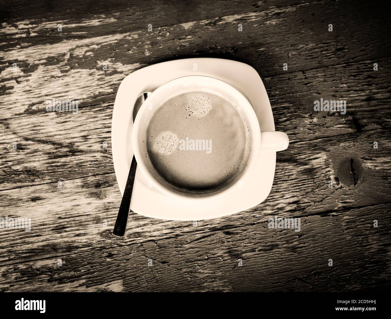 Black and white view of fresh cup of coffee on a weathered table from above Stock Photo