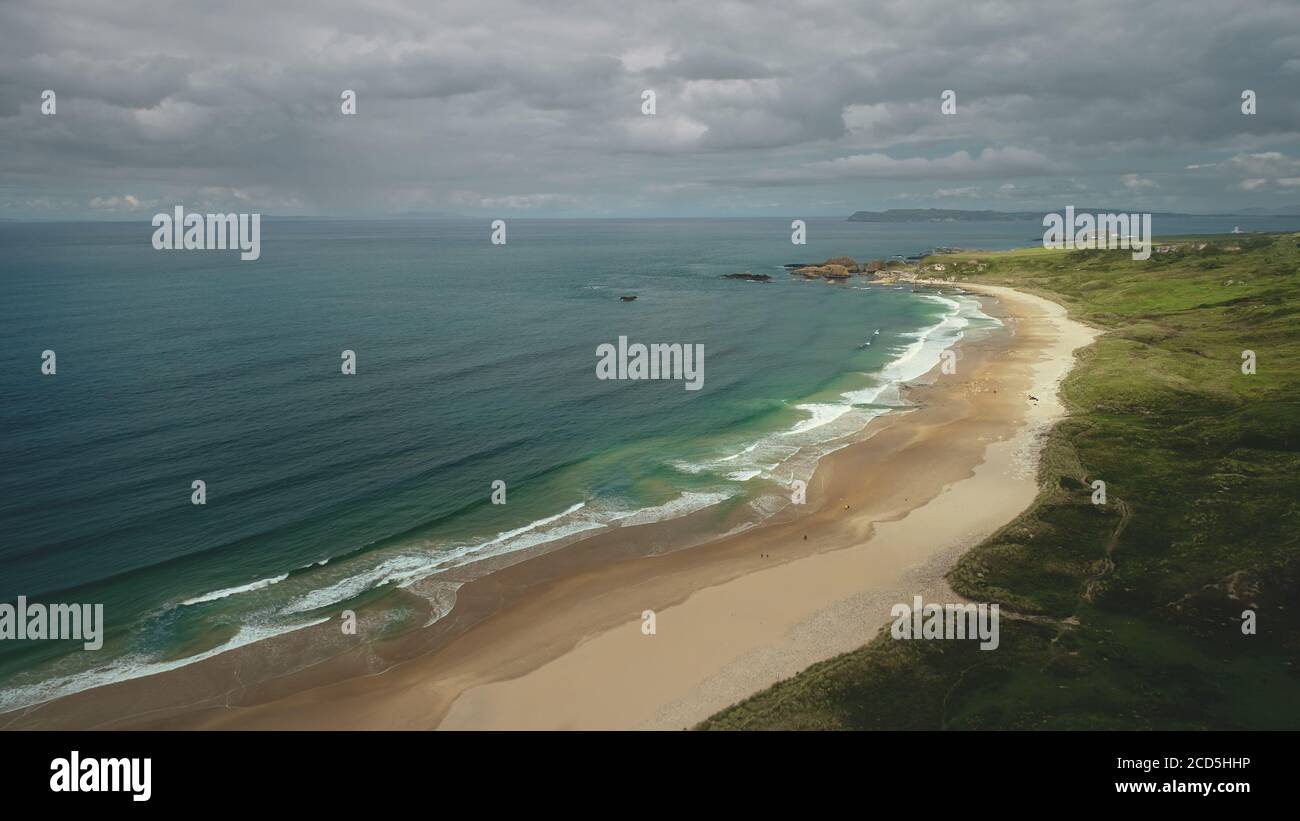 Aerial view sandy beach: ocean foamy waves drops to coastline in White Beach, Antrim County. Seascape of picturesque nature of Northern Ireland. Dramatic summer scenery in day Stock Photo
