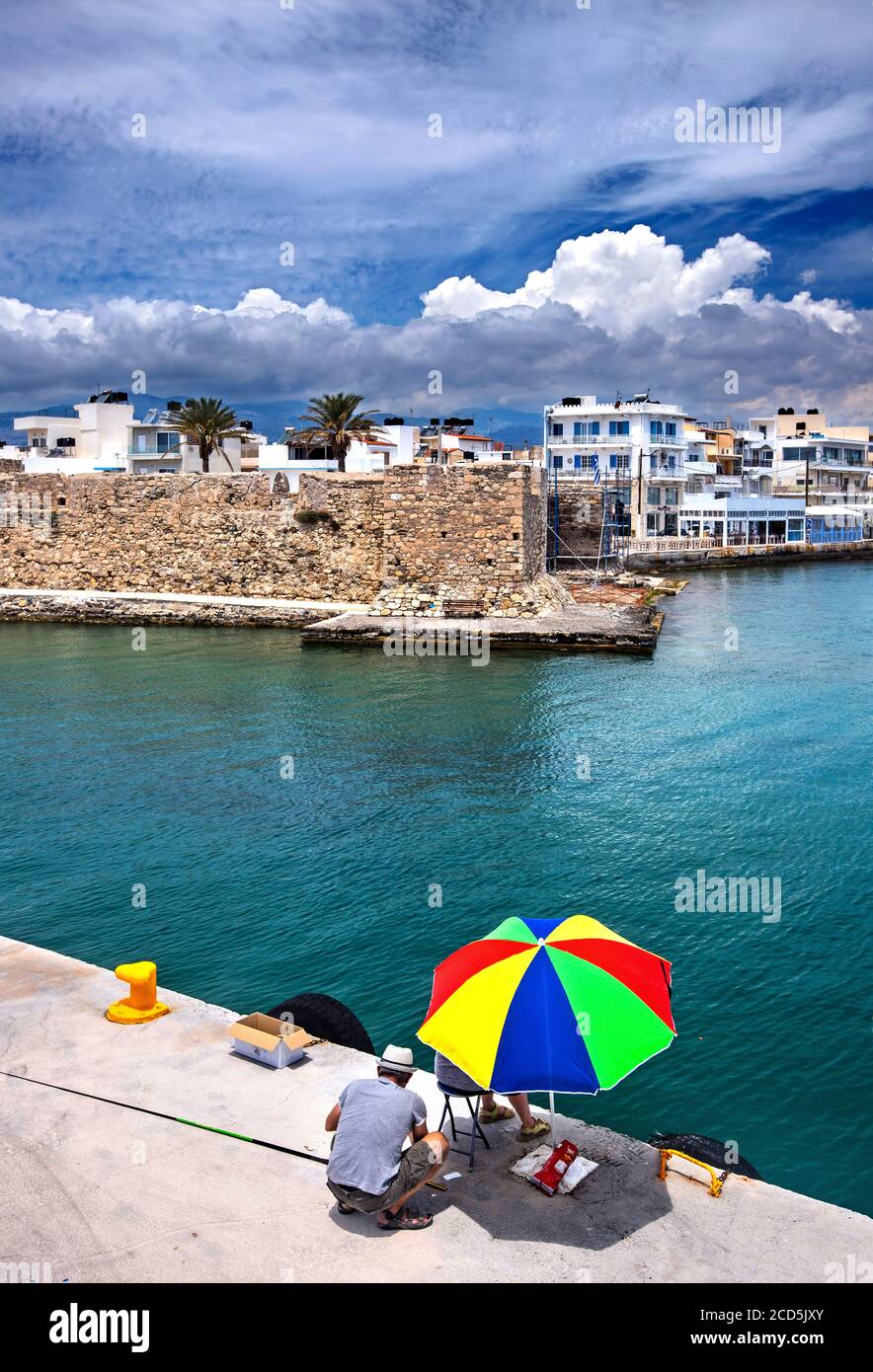 People fishing at the entrance of the old port of ierapetra town, Crete, Greece. In the background Kales castle. Stock Photo