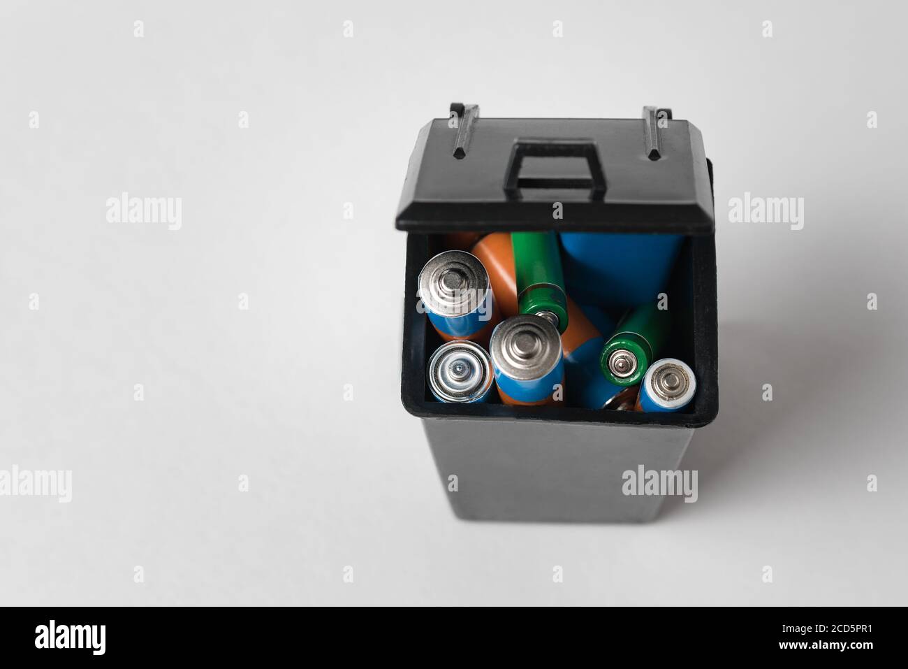 Alkaline batteries in black garbage container on white background