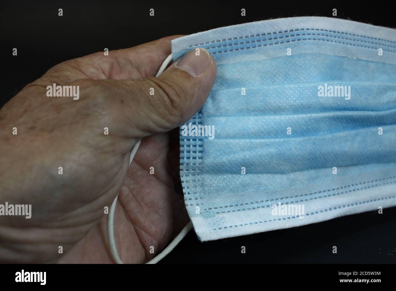 Person's hand holding a face mask isolated on black background ...