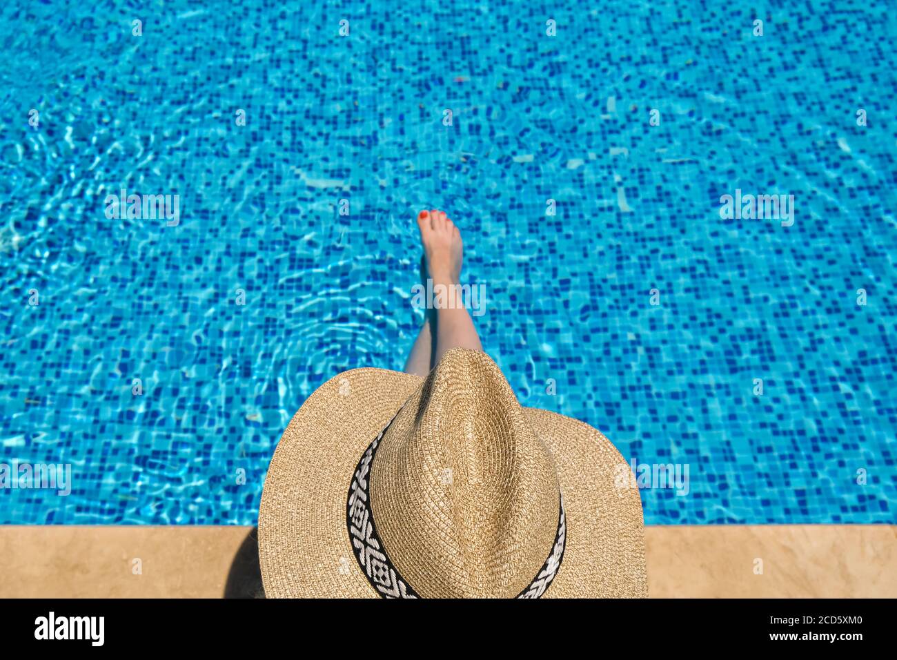 Young woman in straw hat sunbathing sitting on the edge of swimming ...