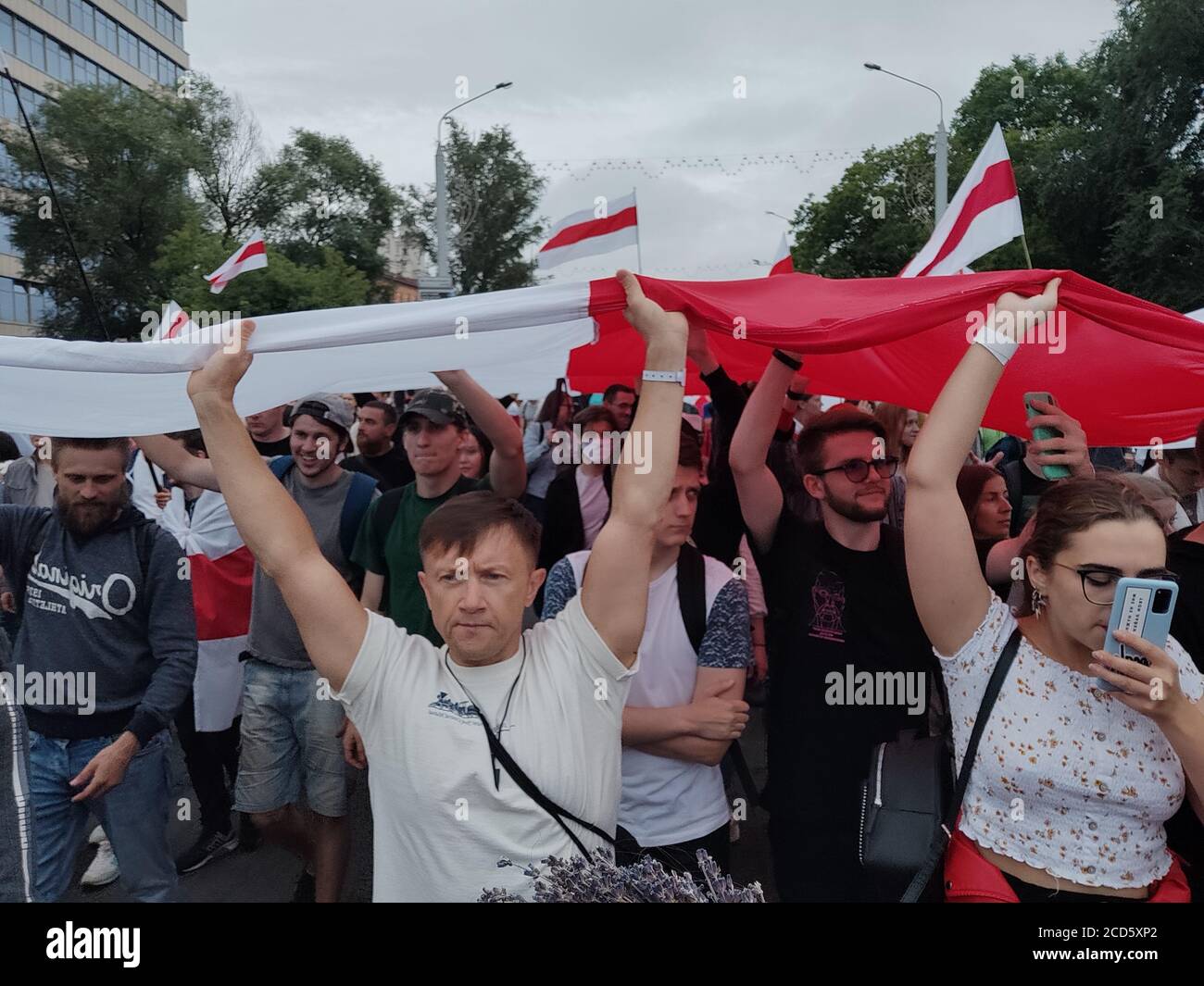 Minsk / Belarus - August 23 2020: Protesters carrying huge white-red-white flag while marching from the Independence Square to the Stella WW2 memorial Stock Photo
