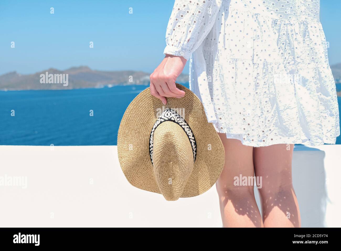 Beautiful woman with straw hat in hand in white dress sunglasses on white terrace of villa hotel resort Sea View Stock Photo