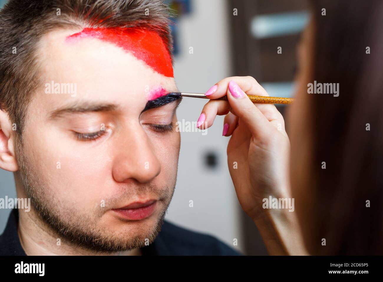 Girl artist paints on a mans face. Face painting on the skin. Portrait of a young man with
