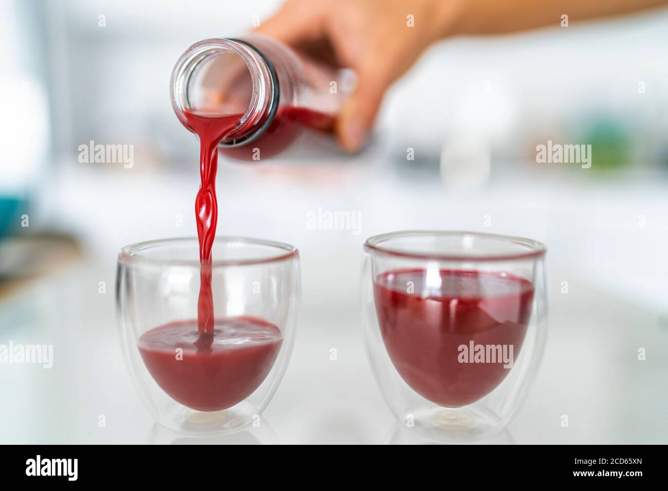 Juice bottle beet drink smoothie woman pouring drinks in cups at home kitchen. Closeup of two glasses with red vegetable juicing cold pressed beverage Stock Photo