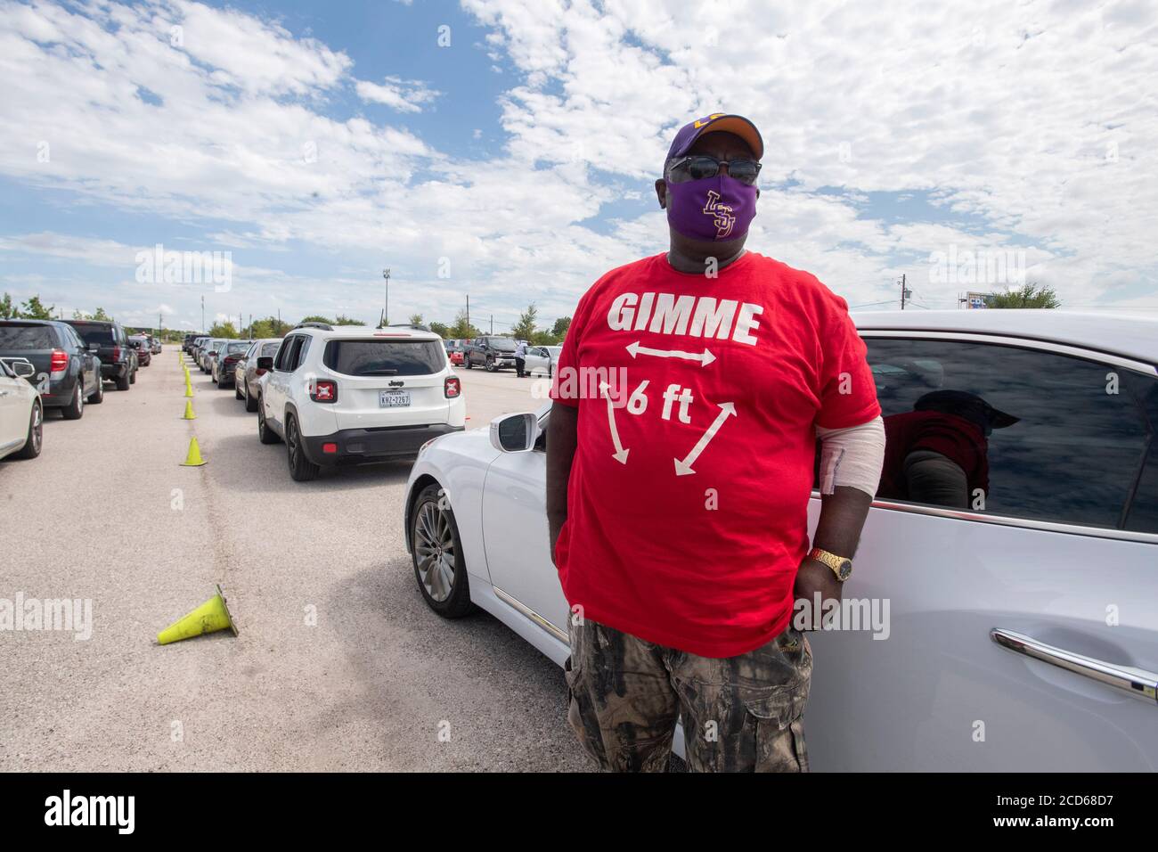 Austin, TX USA August 26, 2020: Hundreds of cars from coastal east Texas and southwest Louisiana wait in line at a Hurricane Laura evacuation center at the Circuit of the Americas race track parking areas. After spending hours in his car, Ronnie Ruffin of Lake Charles, LA, gets some fresh air while wearing a mask and a 'Gimme 6 feet' tee shirt. Laura is expected to make landfall overnight as a Category 4 storm and wreak havoc along the Texas and Louisiana coasts and inland. Credit: Bob Daemmrich/Alamy Live News Stock Photo