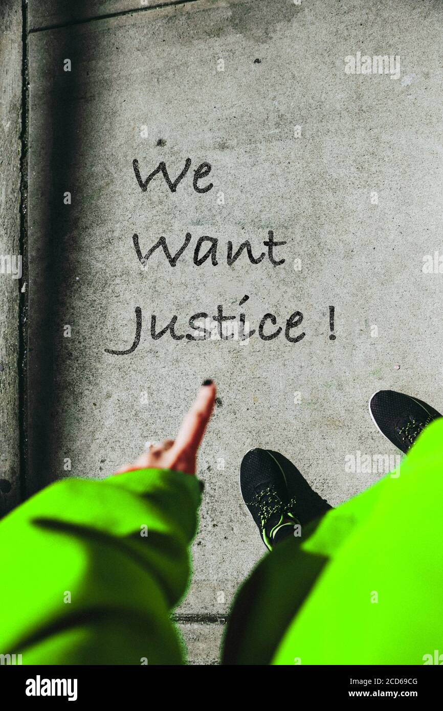 A girl with Green dress pointing at 'We want Justice !' Written on concrete floor. Stock Photo