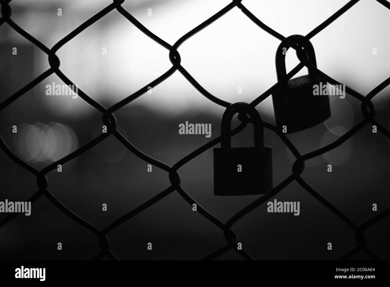 Silhouette of two pad locks on chain link fence against bright background. Stock Photo