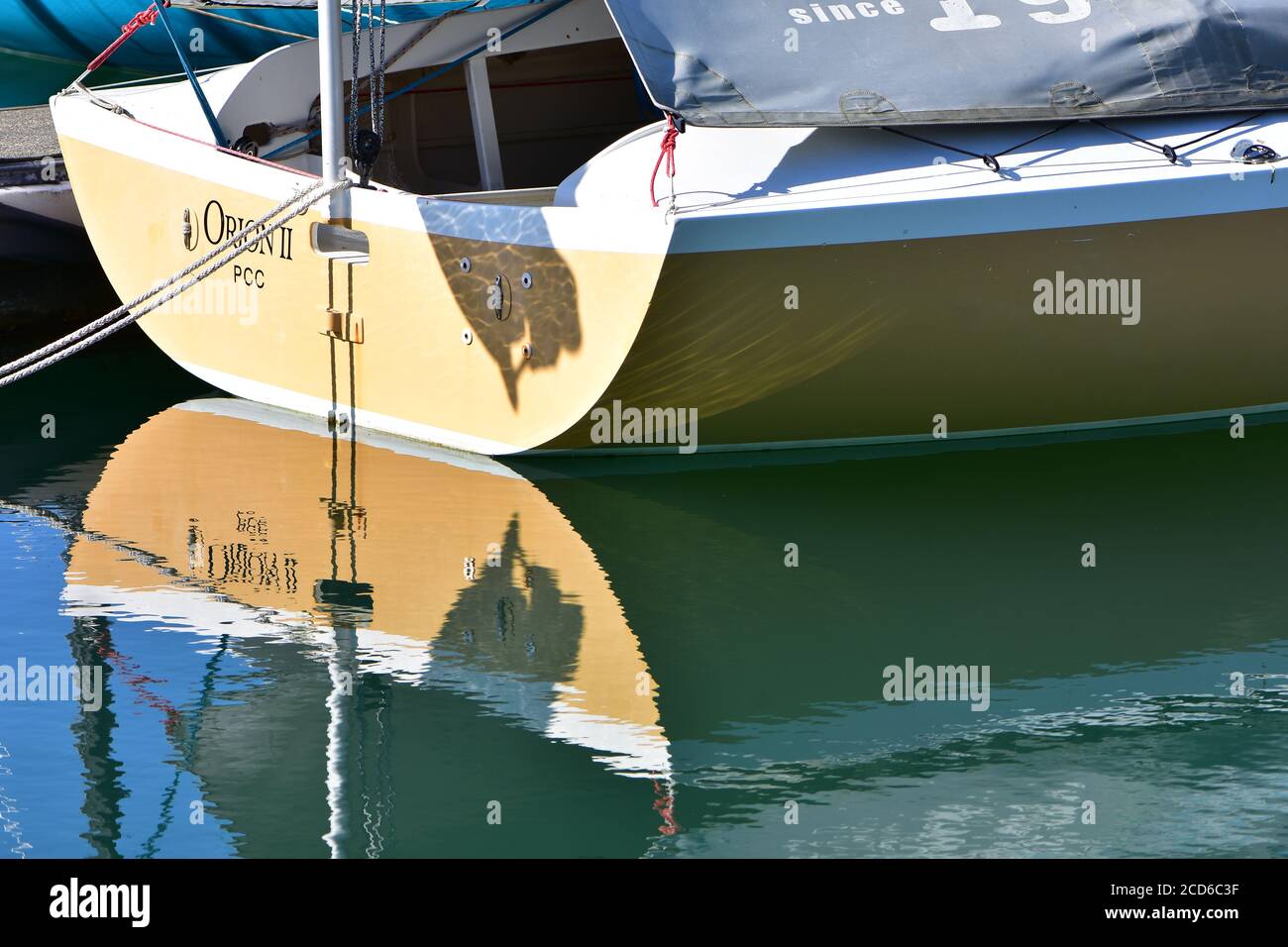 Stern of small sailboat covered with canvas reflecting on calm water surface. Stock Photo