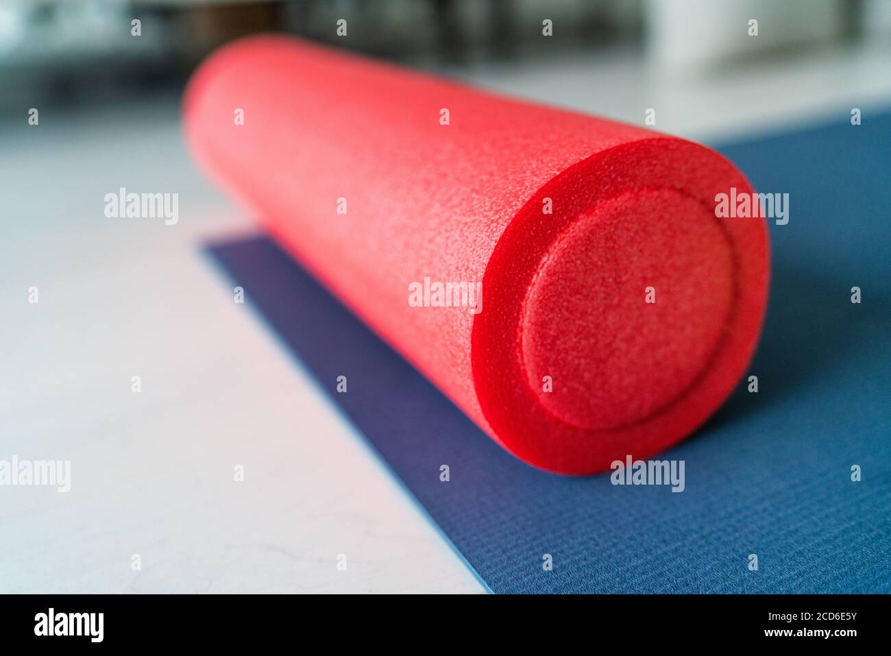 Foam roller fitness equipment on exercise mat gym floor. Indoors closeup of sports object, accessory for athletes to massage tired and tense muscles Stock Photo