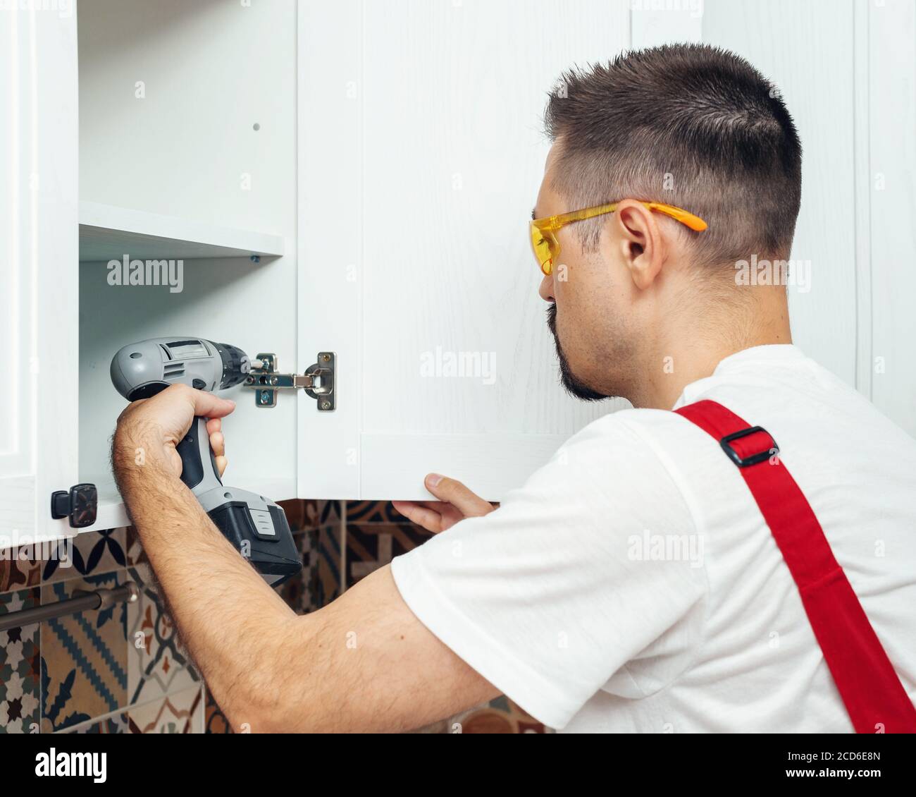 Service contractor using electric screwdriver while installing new furniture in kitchen Stock Photo
