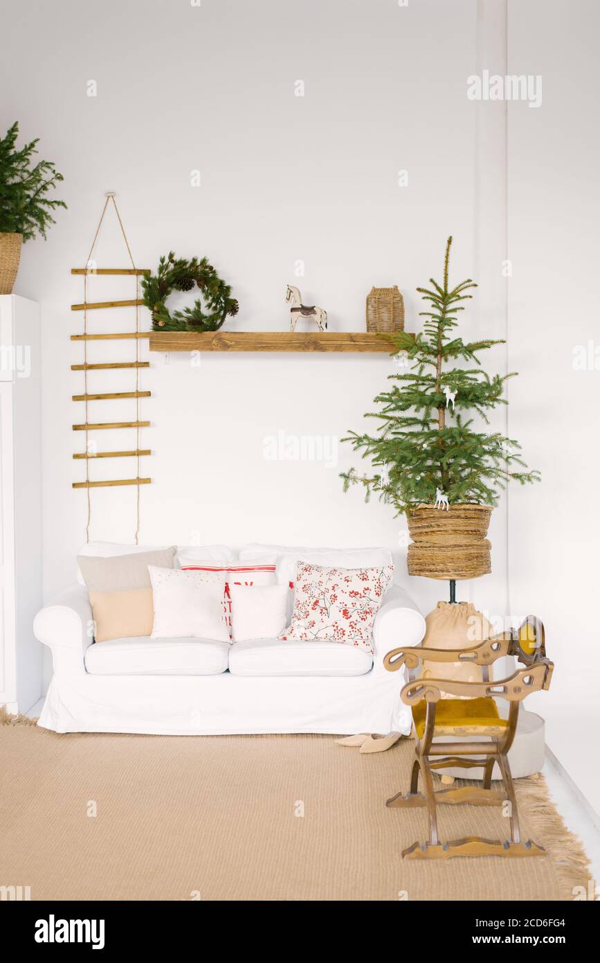Stylish Scandinavian decor in the living room for Christmas or New Year: a white sofa with pillows, a Christmas tree, a wooden rocking chair, Souvenir Stock Photo