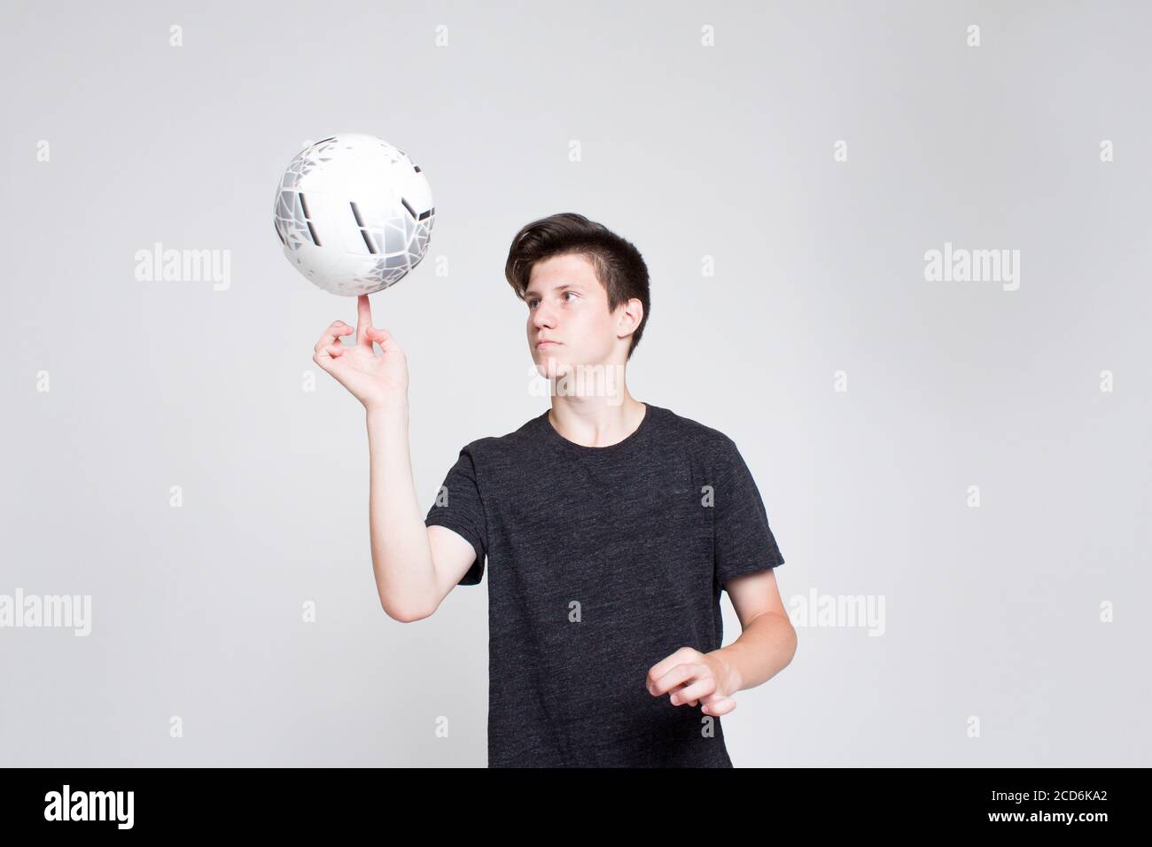 A young guy in a black sports tshirt and shorts, holding a football on