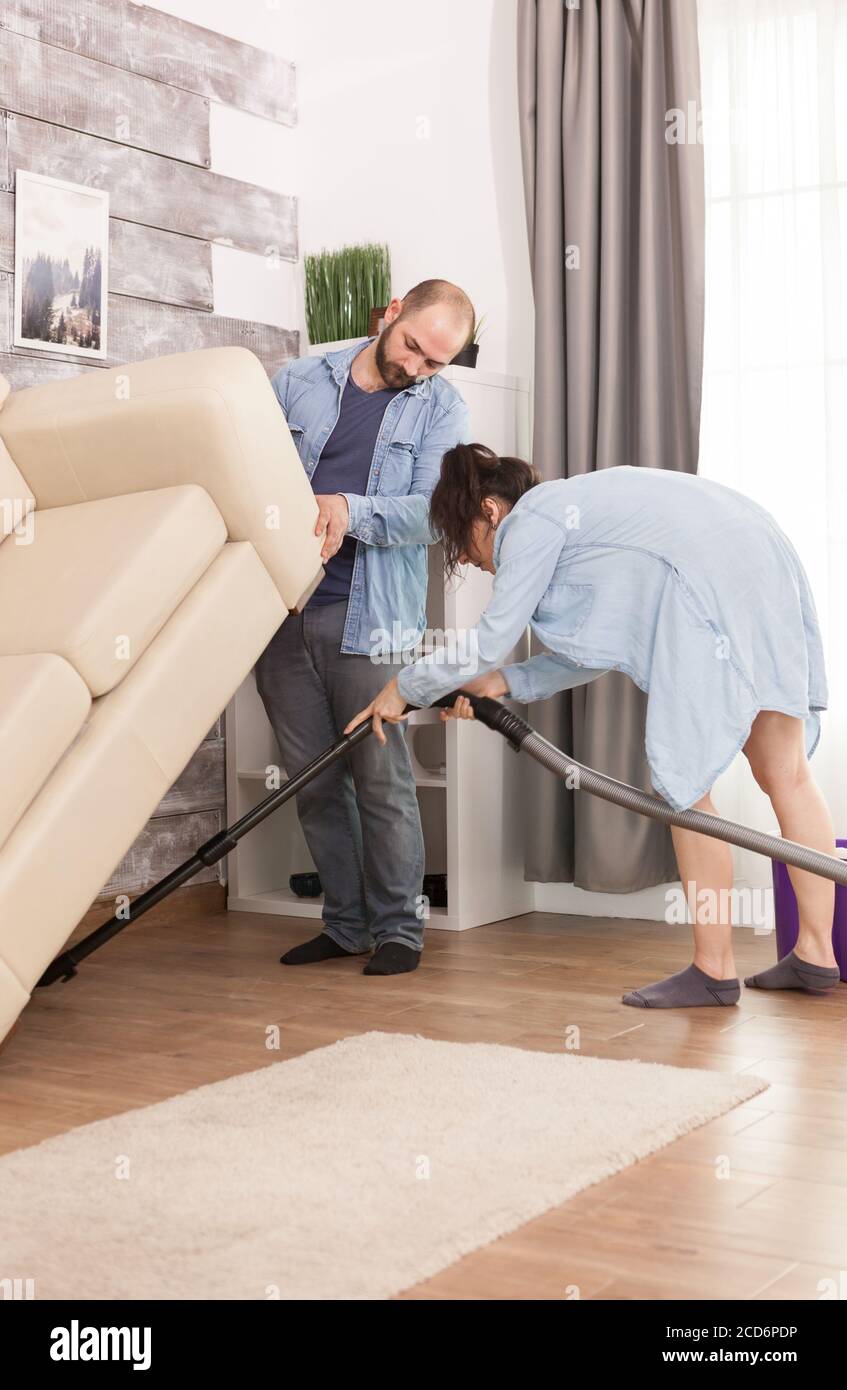 Wife cleaning dust with vacuum cleaner under couch Stock Photo Alamy