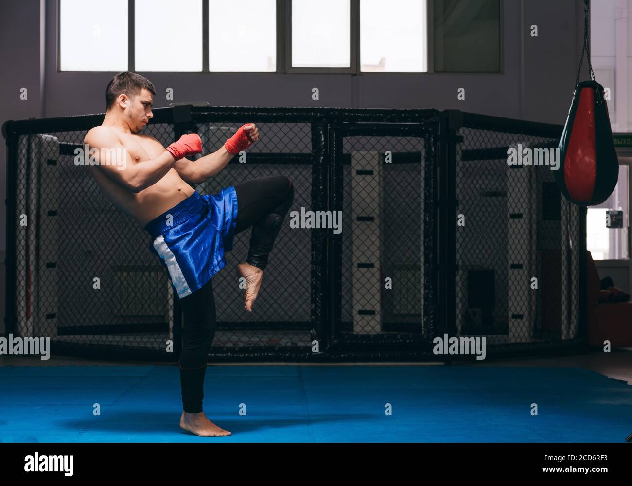 Young athletic man preparing for kickboxing competitions, warming up in gym making kicks with leg during workout Stock Photo