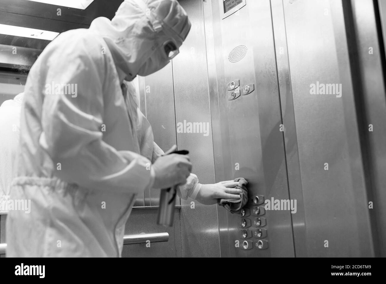 Coronavirus infection. Paramedic in protective mask and costume disinfecting an elevator with sprayer, Stock Photo