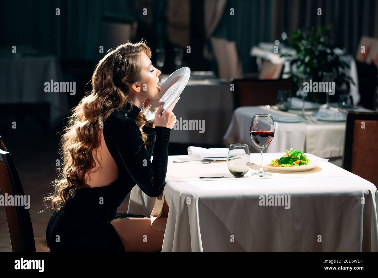 A young woman licks a plate in a restaurant. Stock Photo