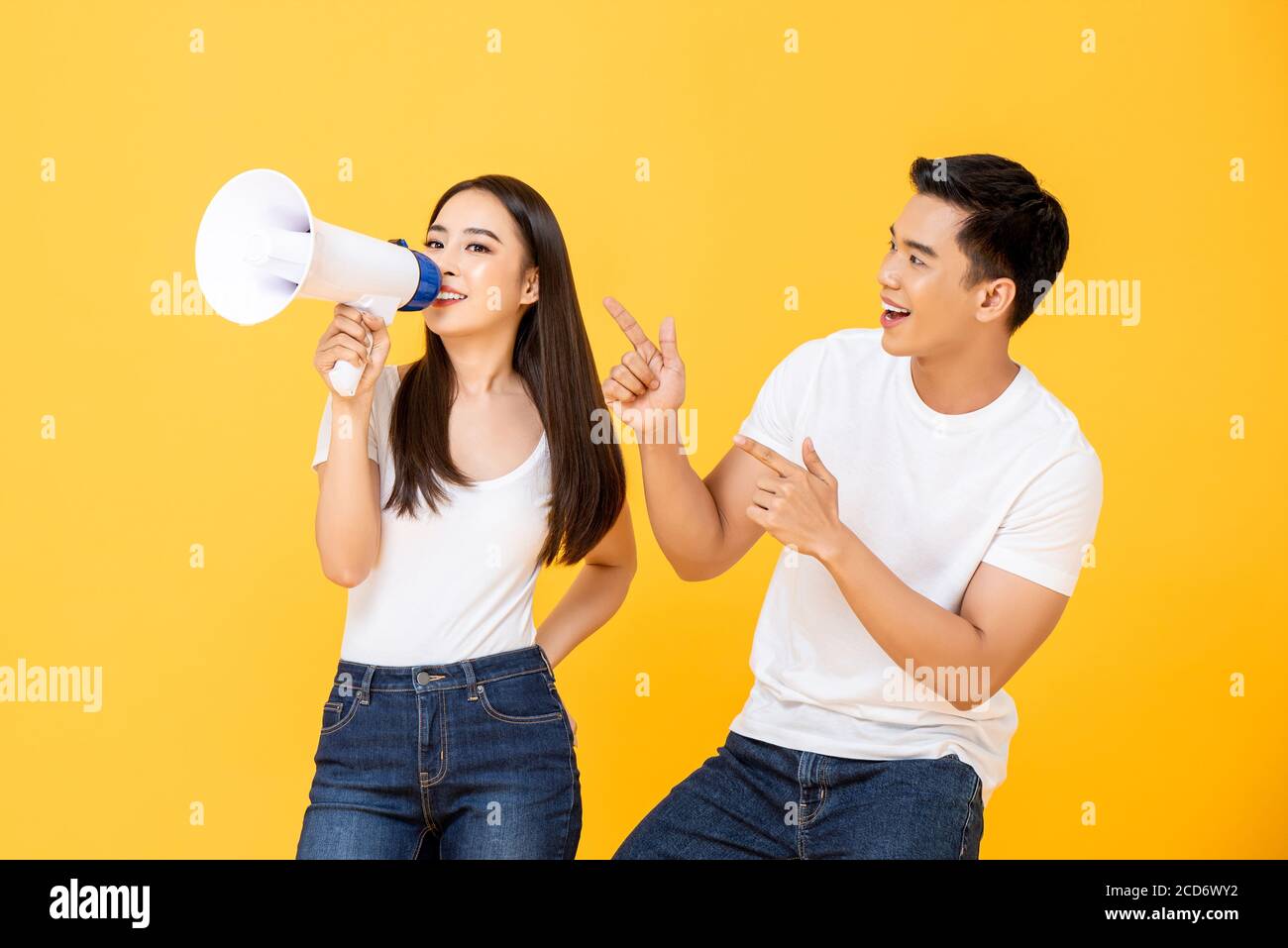 Fun portrait of happy young Asian couple making announcement in isolated studio yellow background Stock Photo