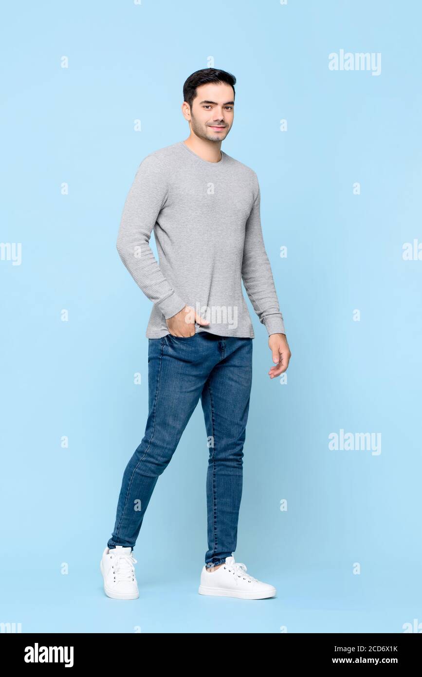 Full length portrait of young handsome Caucasian man standing with hand in pocket while looking at camera in isolated studio blue background Stock Photo