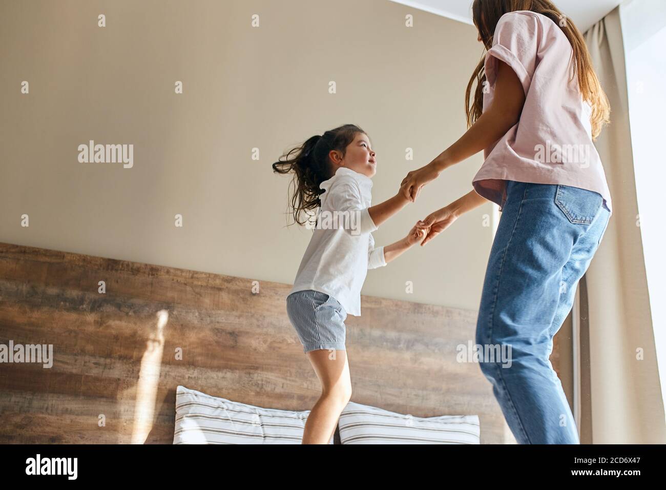 Young mother and little daughter having fun at home, playing together, jumping on bed, spending holidays together, family time concept Stock Photo