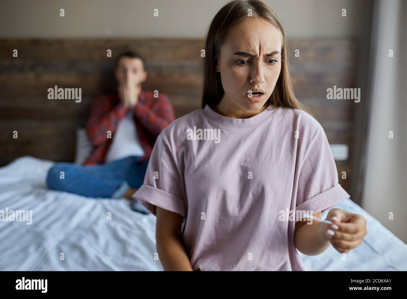 Frustrated young pretty girl knitting her brows with horrified expression, stares at pregnancy test, gets positive result, looks away with shocked emo Stock Photo