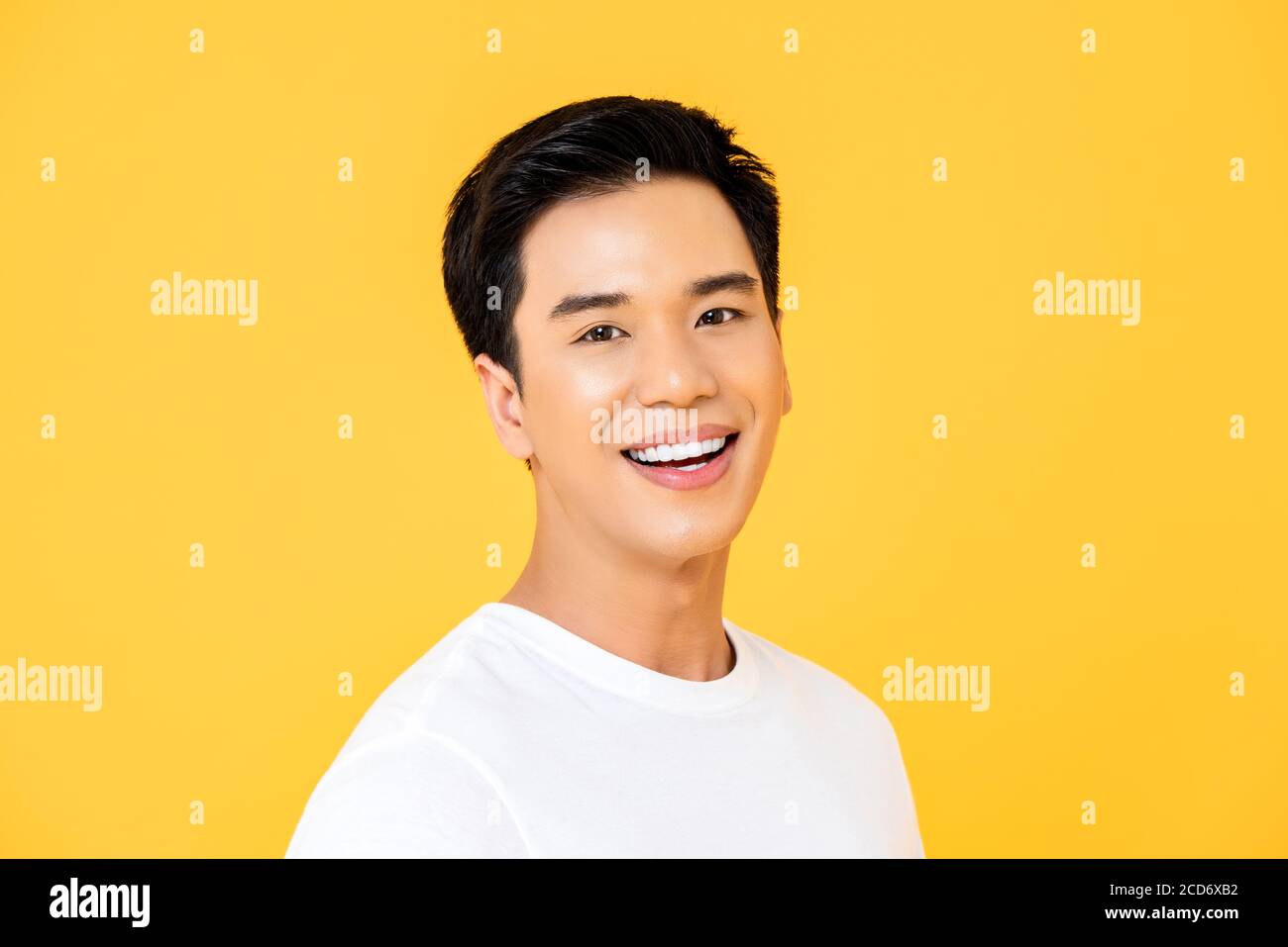 Close up portrait of young handsome Asian man cheerfuly smiling and looking at camera in isolated studio yellow background Stock Photo
