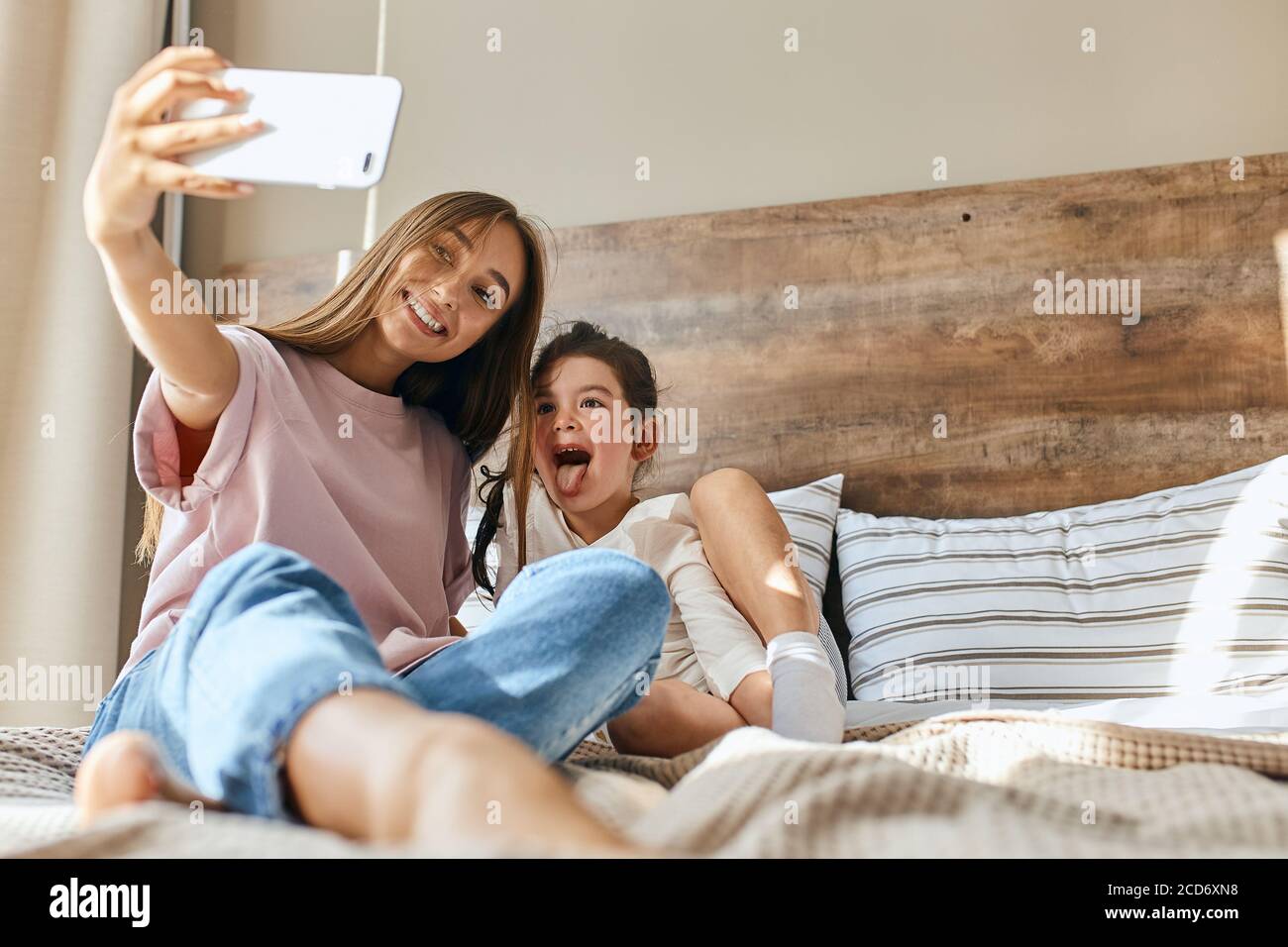 Happy loving family. mother and child girl playing, hugging, taking photo on cell phone, lying on bed, looking away, happy morning time concept, botto Stock Photo